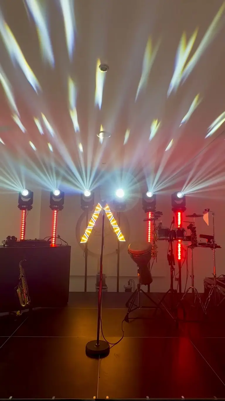 Sei teste mobili aprono un ventaglio di fasci sopra un palco con batteria, sax e barre LED