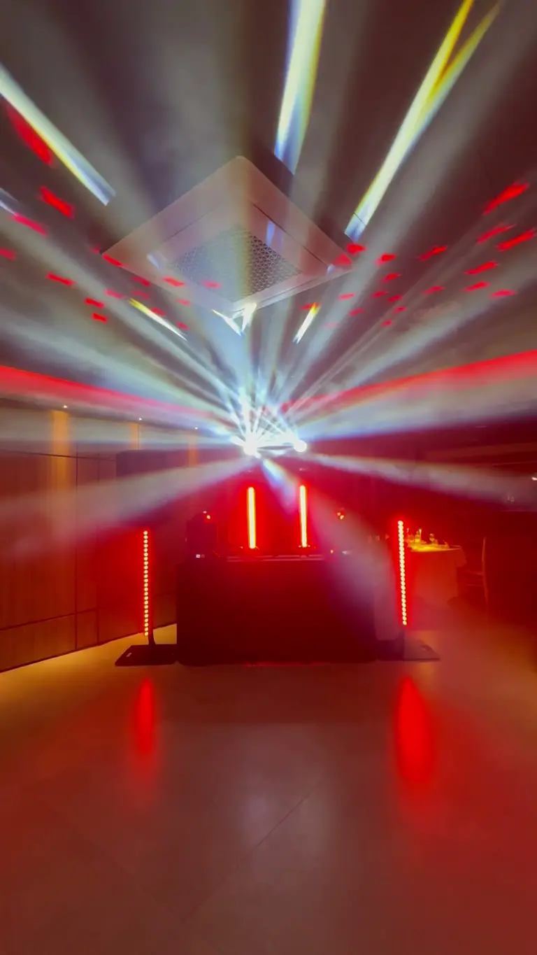 Postazione DJ con barre LED rosse e un ventaglio di fasci che si apre sul soffitto della sala