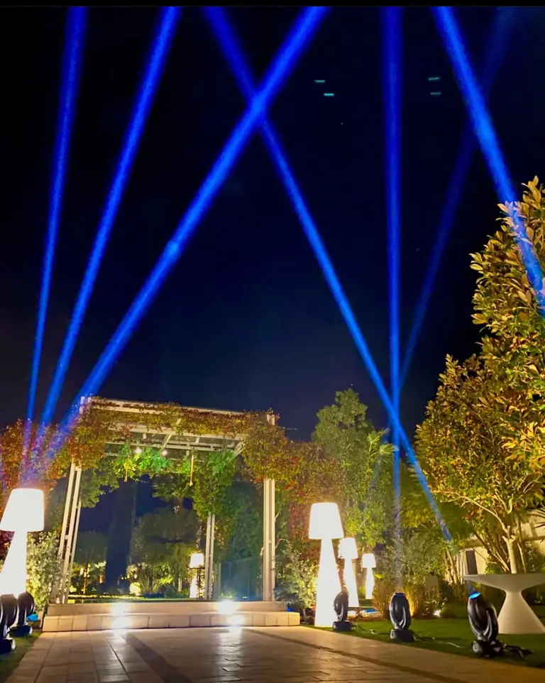 Giardino con fasci di luce blu che si incrociano sopra un pergolato