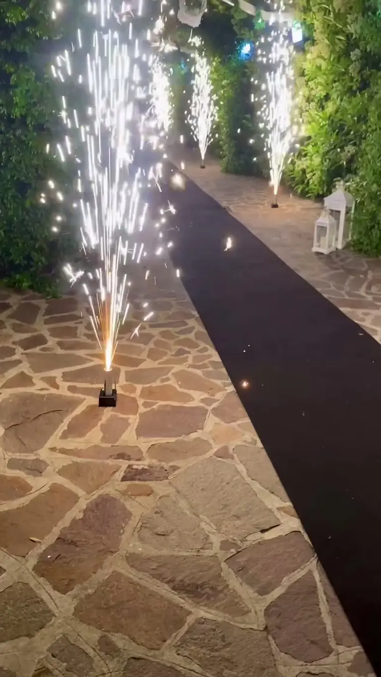 Passerella delimitata da fontane di scintille fredde tra siepi illuminate e lanterne