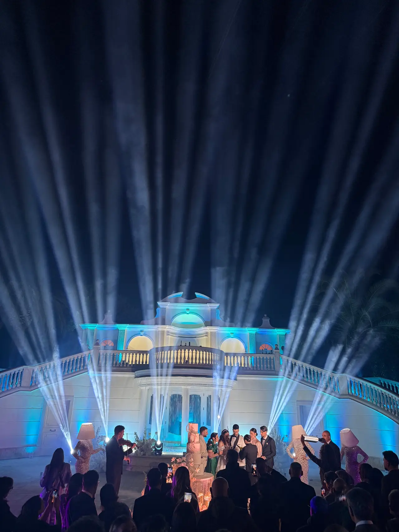Villa illuminata da FC Service con fasci di luce blu che si aprono nel cielo notturno durante un ricevimento