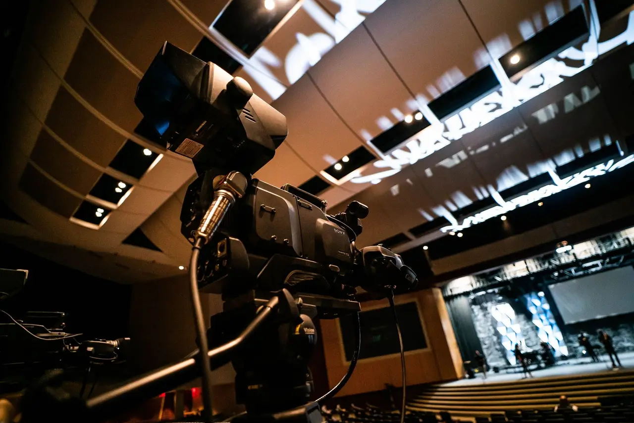 Telecamera professionale su treppiede in un auditorium, palco e schermo sullo sfondo